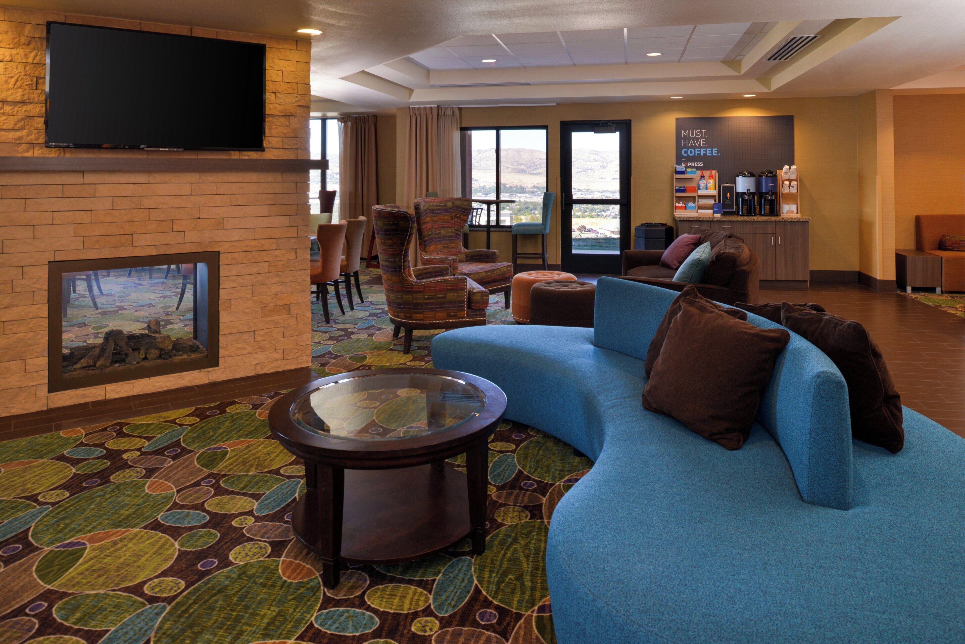 A hotel lobby with a large blue sofa, a coffee station, and a television mounted on a brick wall.