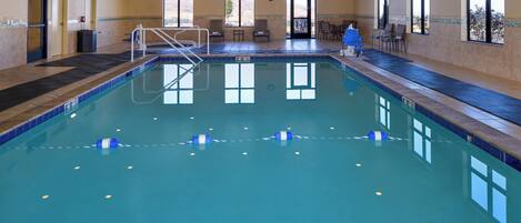 Piscina interna com água cristalina, plataforma de mergulho e área de estar com cadeiras e mesa.