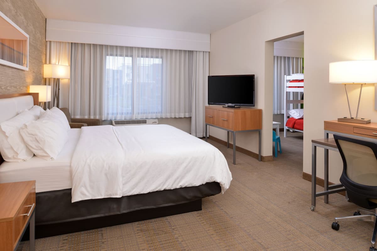 A hotel room with a large bed, a TV, a desk with a chair, and a bathroom visible through an open door.