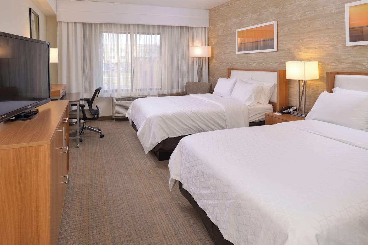 A hotel room with two beds, a desk with a TV, a chair, and a lamp.
