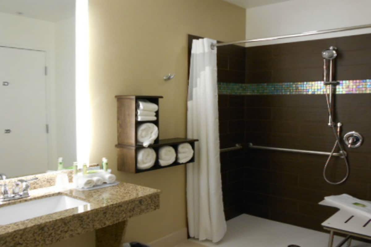 A bathroom with a sink, mirror, shower, and towel rack.