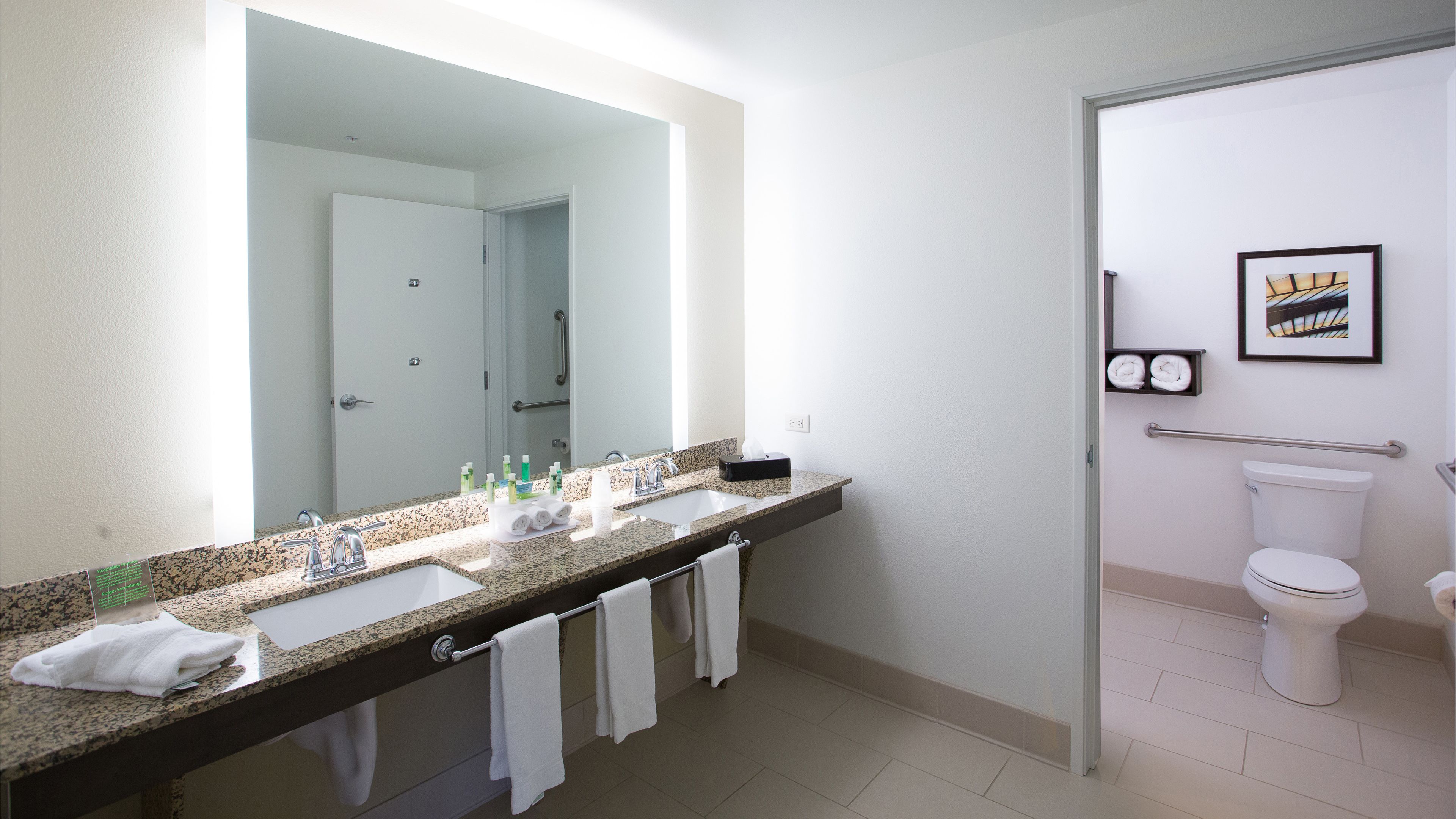 Un baño moderno con dos lavamanos, un espejo grande y un inodoro.