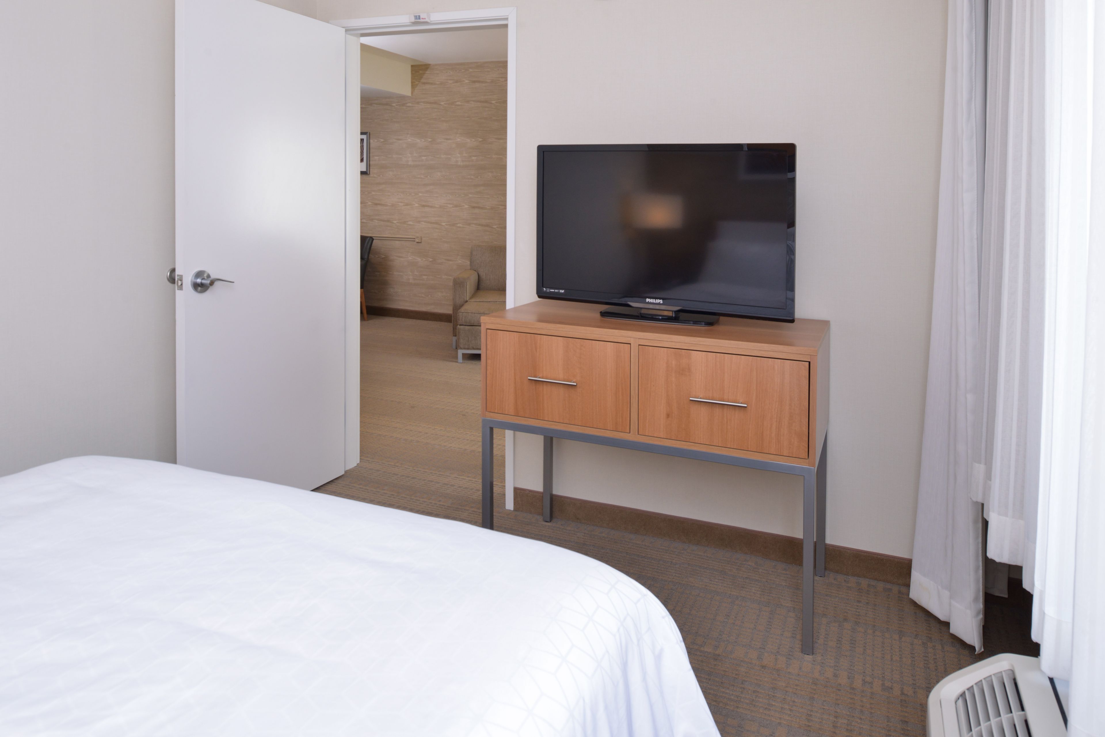A hotel room with a bed, a television on a wooden cabinet, and a door leading to another room.