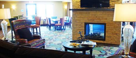 A hotel lobby with a fireplace, seating area, and a television mounted on the wall.