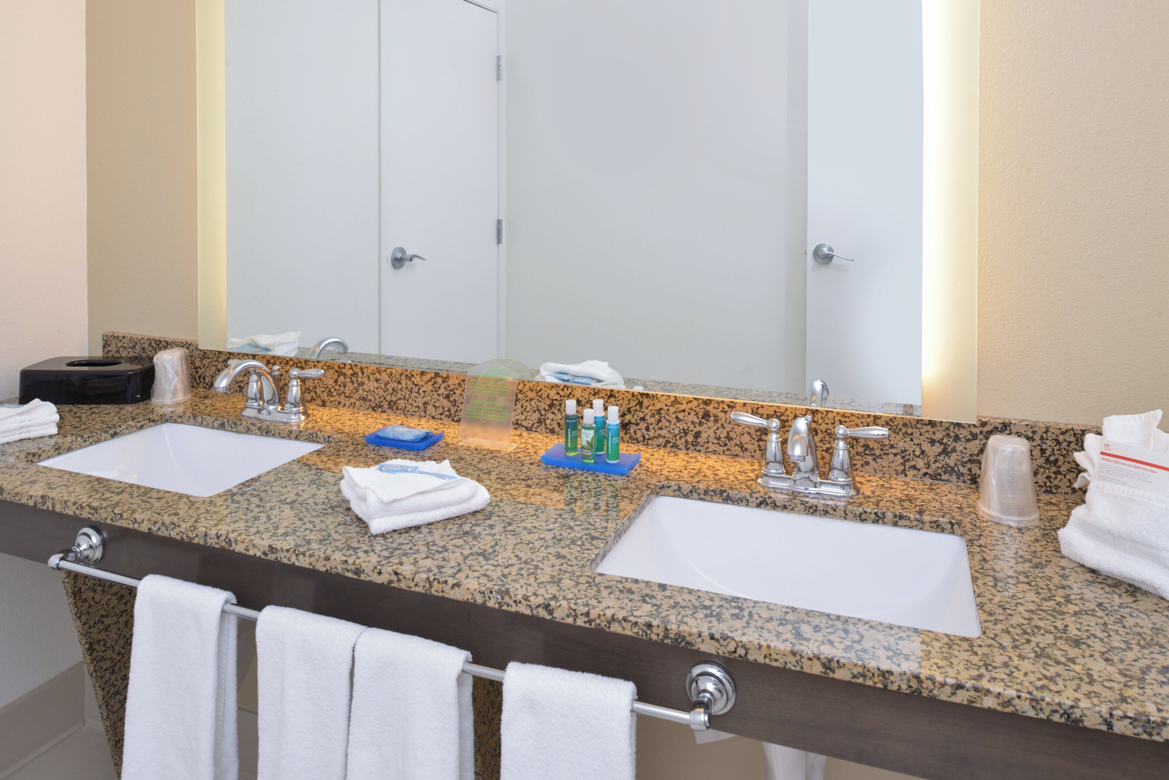 A bathroom with two sinks, a large mirror, and a towel rack with towels.