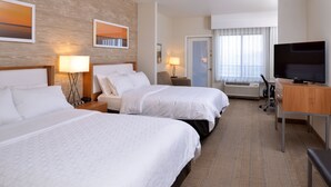 A hotel room with two beds, a TV, a desk, and a window with curtains.