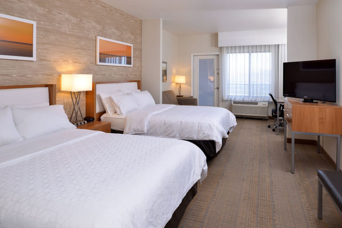 A hotel room with two beds, a TV, a desk, and a window with curtains.