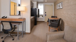 A compact hotel room with a desk, office chair, sofa, and a dining area with chairs.