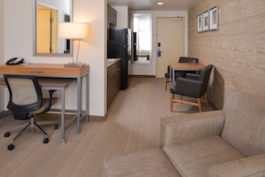 Une chambre d’hôtel compacte comprenant un bureau, un fauteuil de bureau, un canapé et un coin repas avec des chaises.