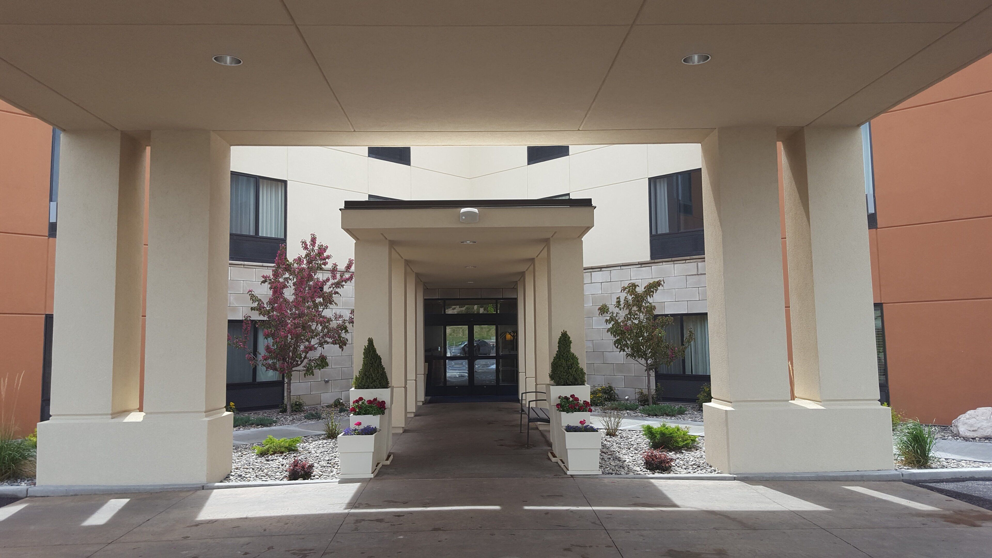 A modern building entrance with a covered walkway, potted plants, and a clear view into the building.