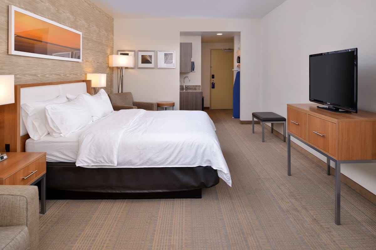 A hotel room with a bed, bedside tables, a television, a desk, and a kitchenette.