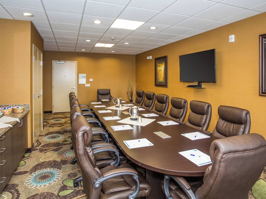 A conference room with a long table, leather chairs, a coffee station, and a television on the wall.