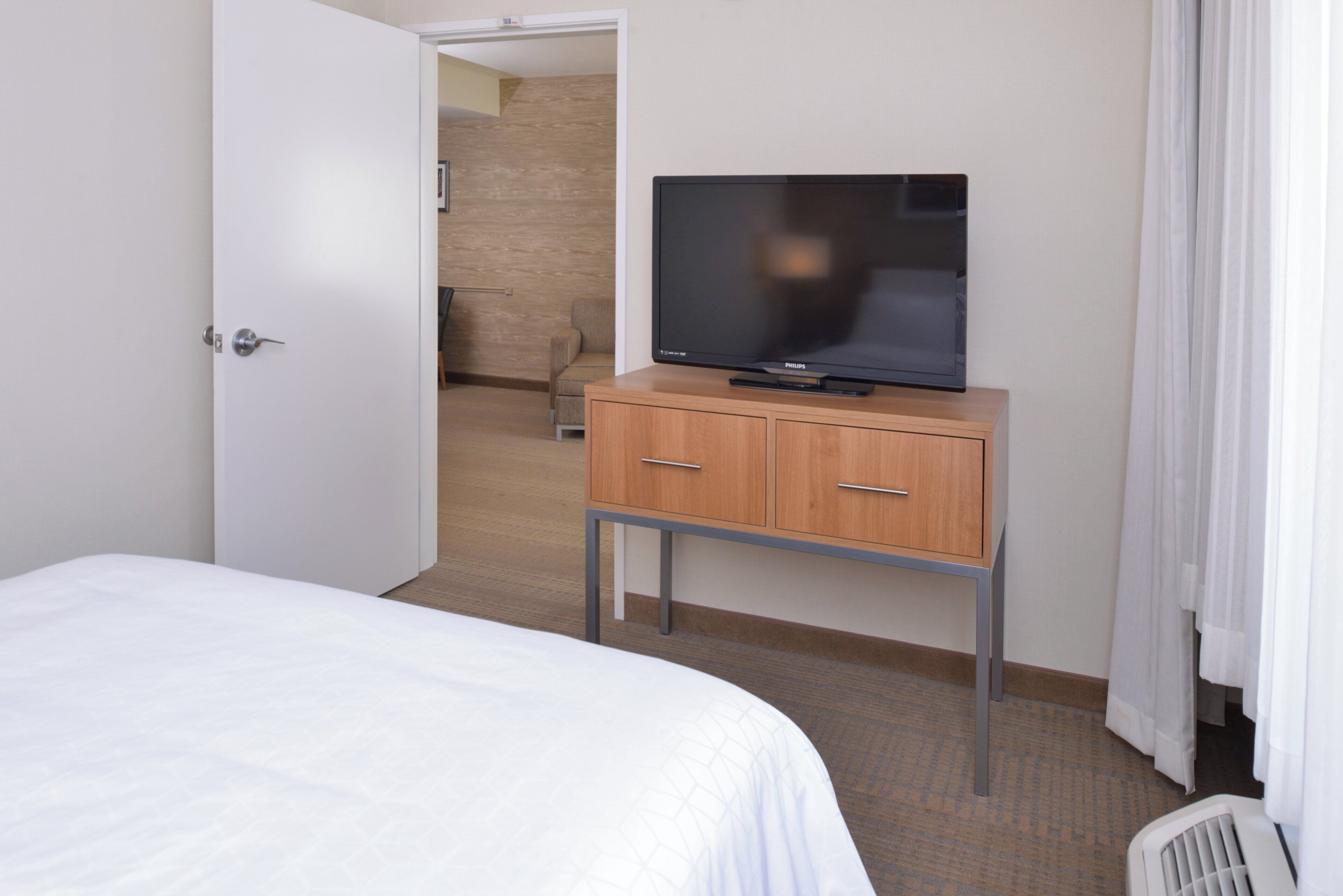 A hotel room with a bed, a television on a wooden cabinet, and a door leading to another room.