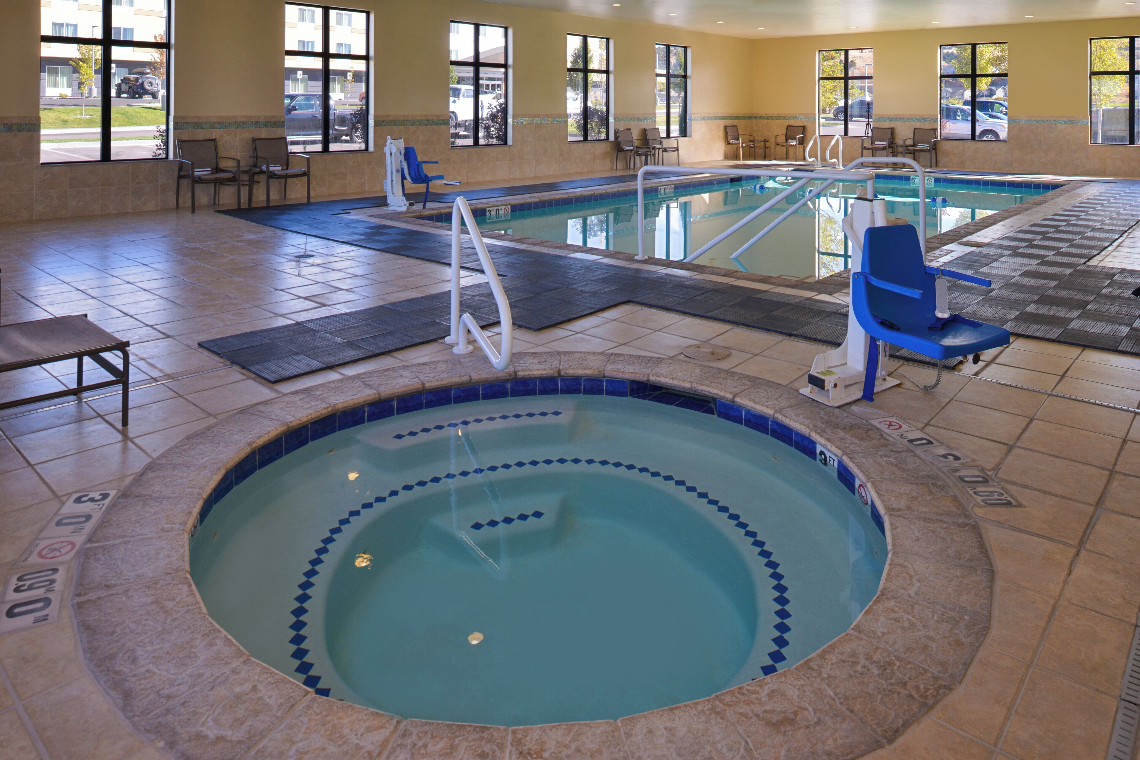 An indoor swimming pool with a hot tub, lounge chairs, and a view of the outside.