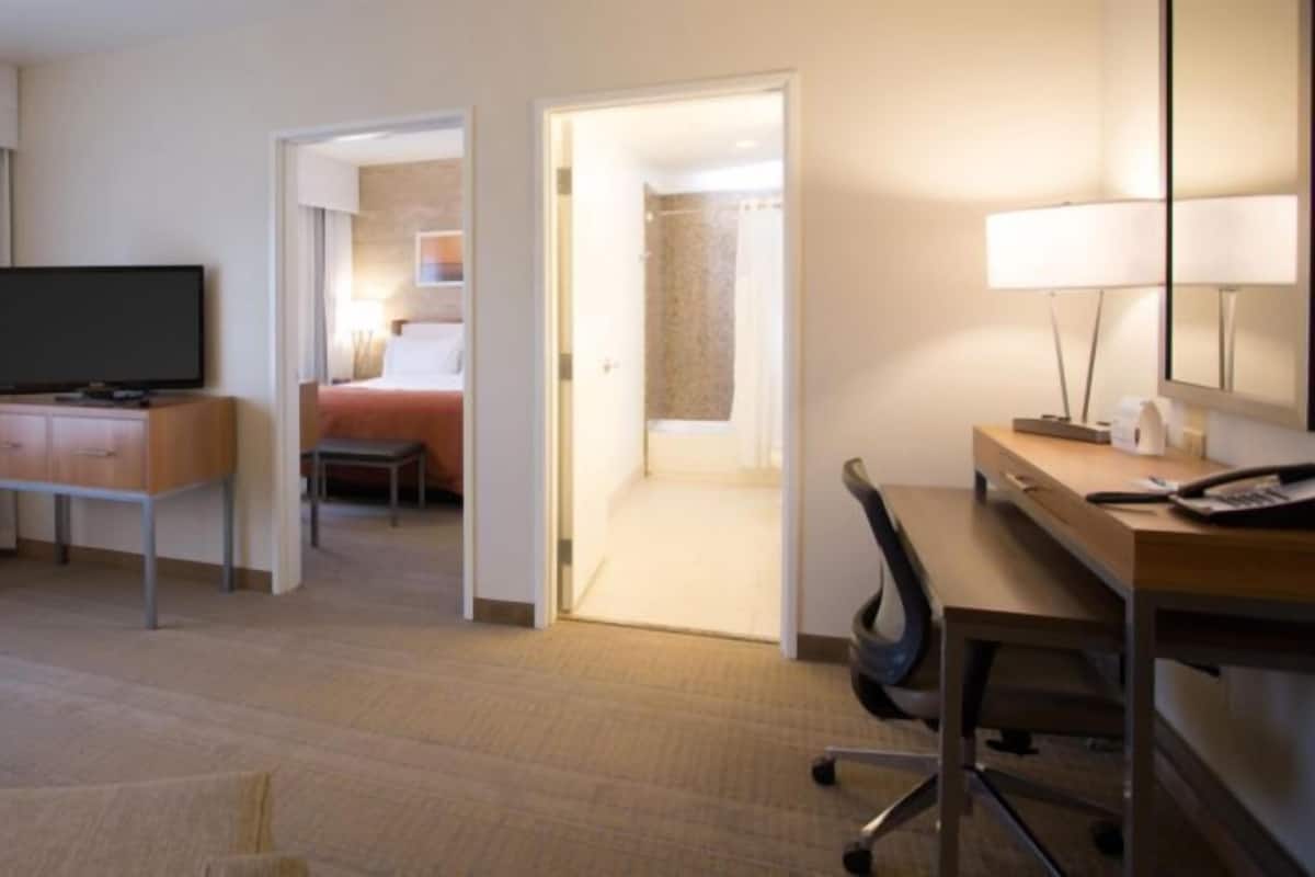 A hotel room with a bed, a desk, a television, and a bathroom visible through an open door.