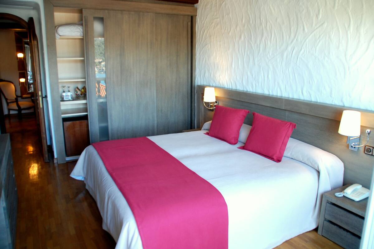 A hotel room with a large bed, two bedside lamps, a nightstand with a phone, and a wooden floor.