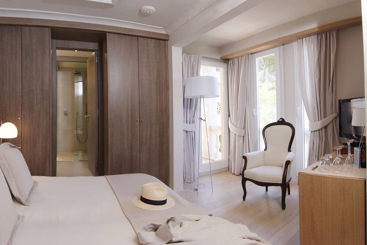 A hotel room with a bed, a chair, a desk with a lamp, and a view of the outdoors.