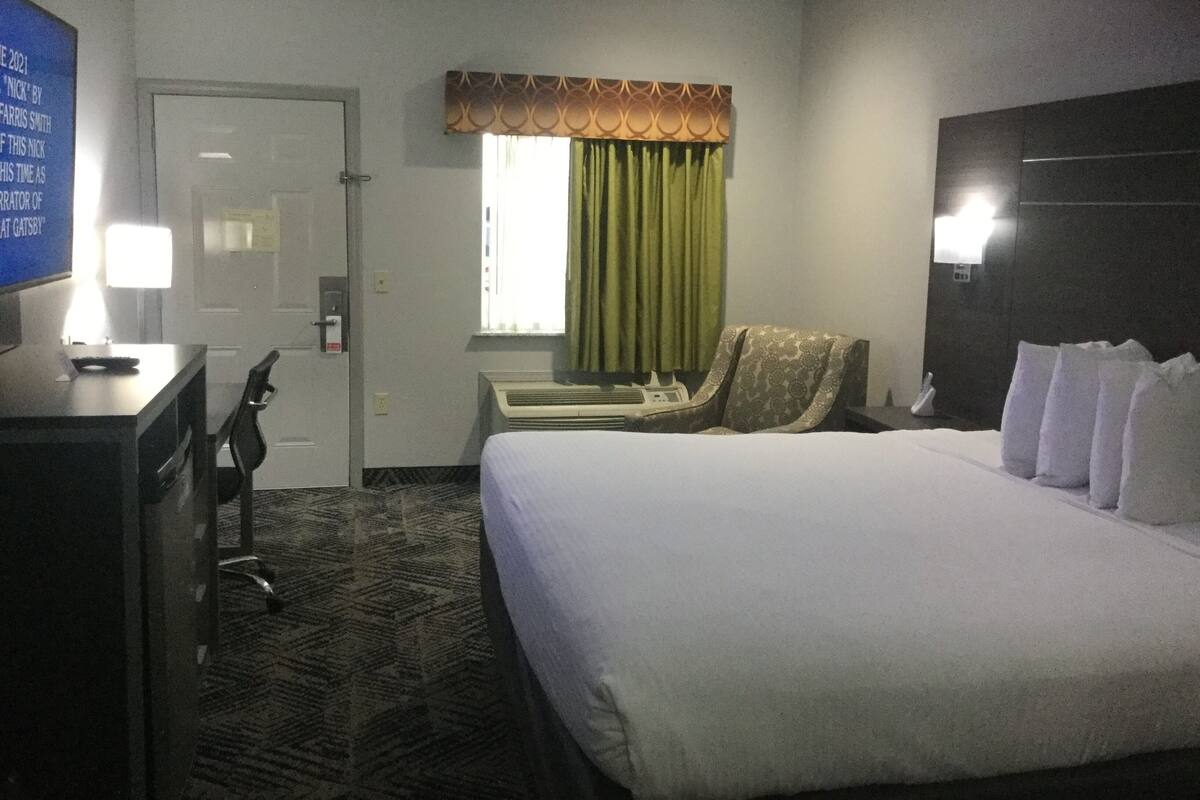 A hotel room with a large bed, a desk with a chair, a window with curtains, and a wall-mounted TV.