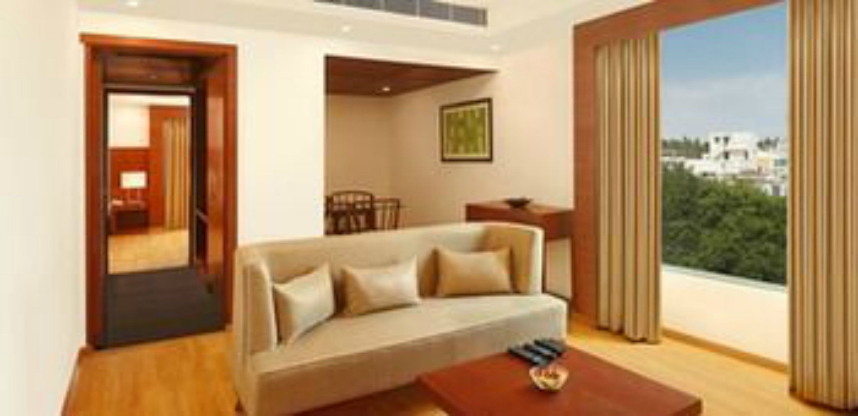 A modern living room with a sofa, a coffee table, and a view of greenery and buildings through large windows.