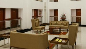 A modern hotel lobby with a sofa set, a coffee table, and a small table with books. - Lemon Tree Hotel Shimona (Chennai)