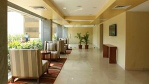 A hotel lobby with a long reception desk, several seating areas with striped chairs, and potted plants. - Lemon Tree Hotel Shimona (Chennai)