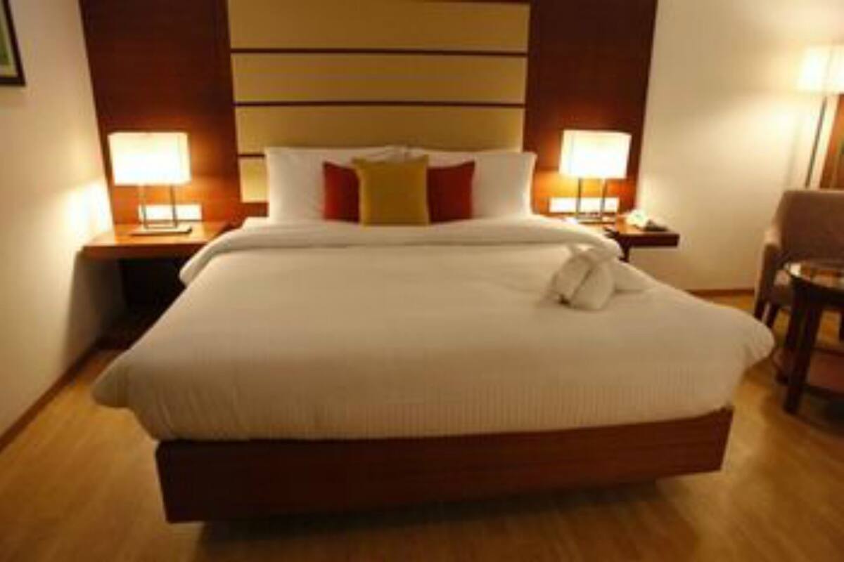 Una habitación de hotel con una cama grande, dos lámparas de noche, un cabecero de madera y una silla.