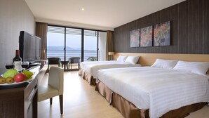 A hotel room with two beds, a TV, a desk with fruit and a bottle, and a view of the sea. - Lealea Garden Hotels - Sun Lake (Yuchi)