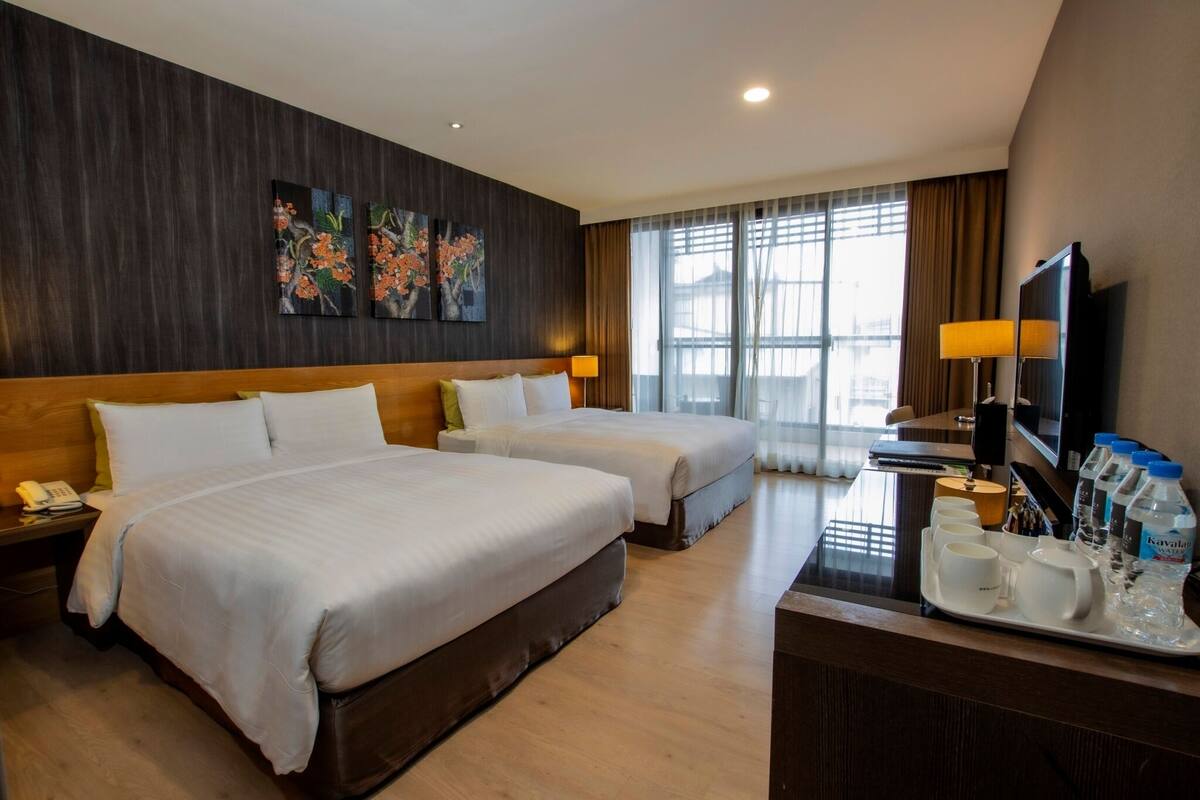 Hotelkamer met twee bedden, een bureau met een dienblad waterflesjes en bekers, een telefoon en kunst aan de muur.