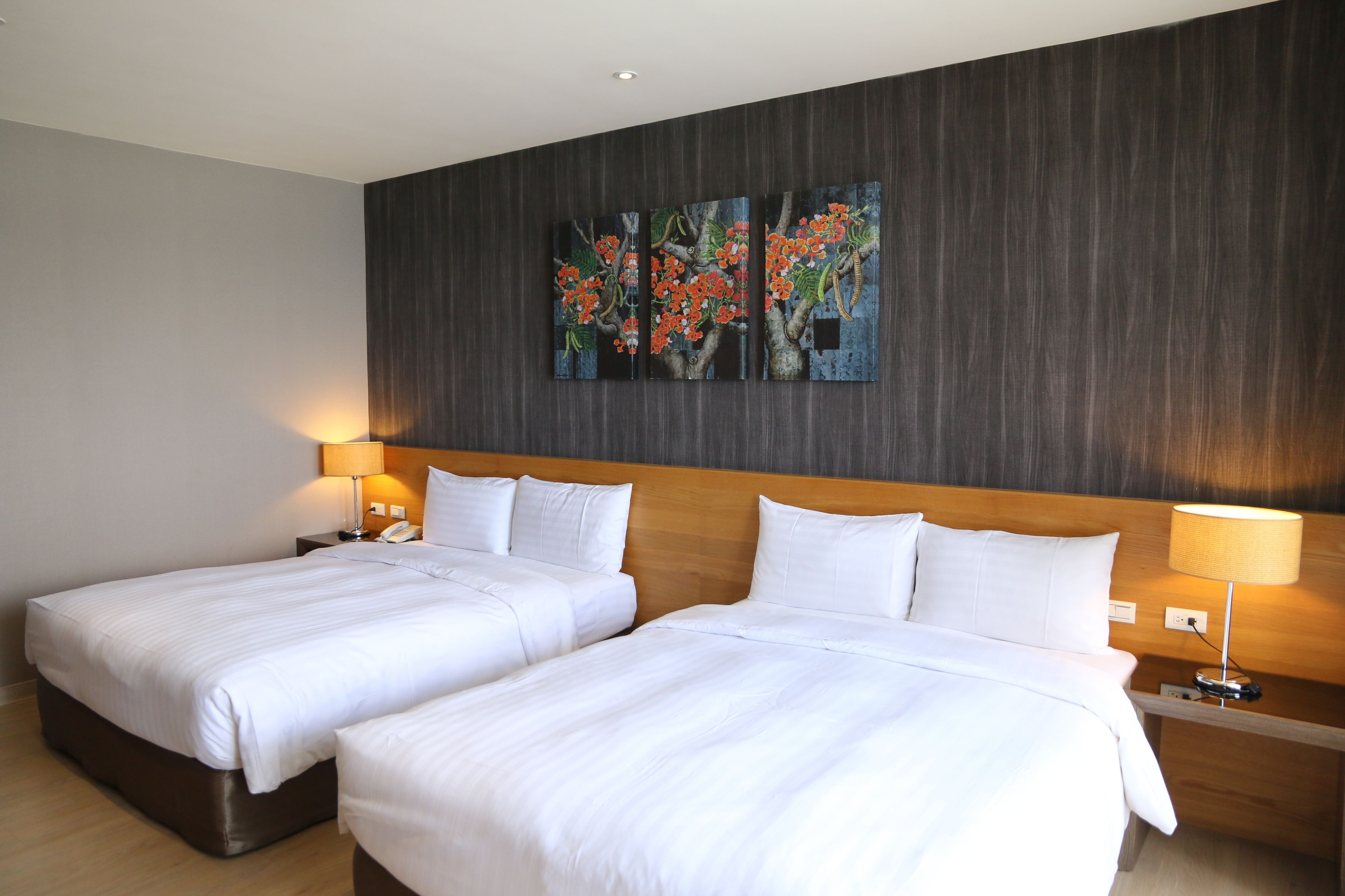 A hotel room with two beds, a wooden headboard, a wall-mounted painting, and bedside lamps.