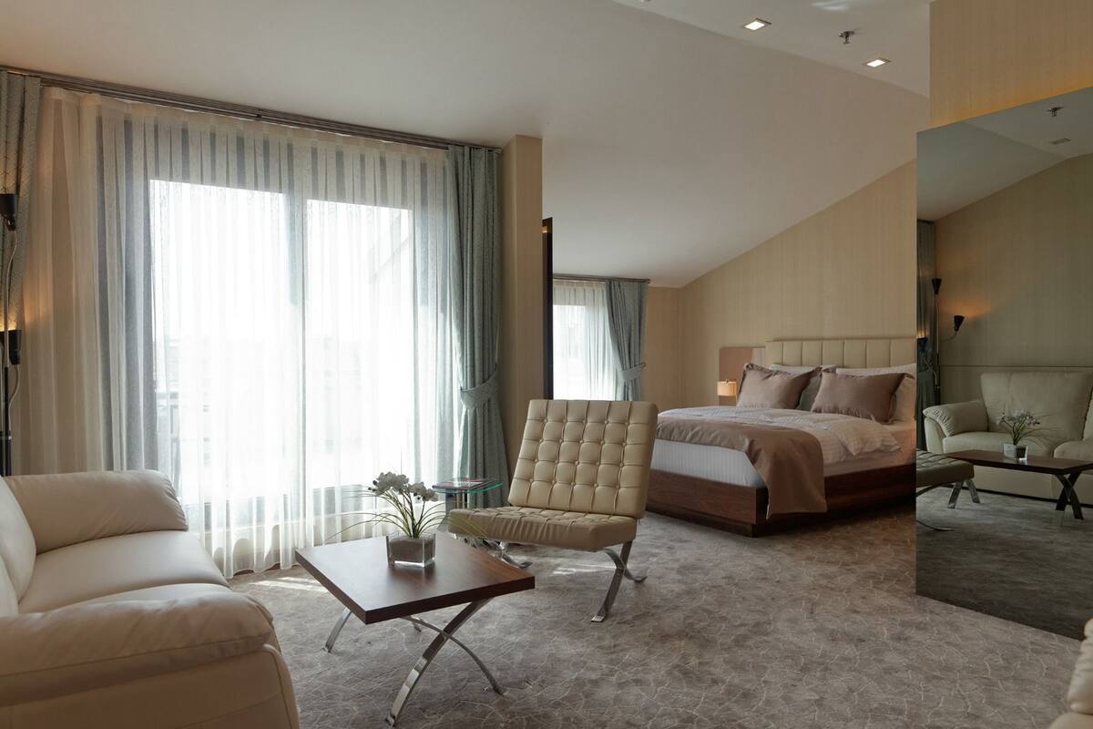 A modern hotel room with a large bed, a seating area with a chair and a table, and a large window with curtains.