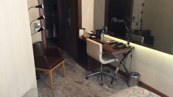 A hotel room with a desk, chair, and a large mirror.