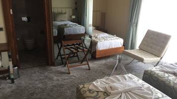 Habitación de hotel con dos camas, una silla de madera, una mesa de vidrio y un otomano estampado.