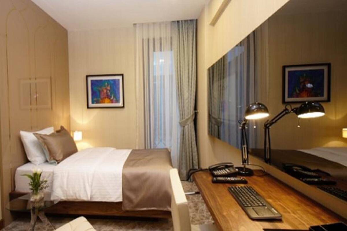 A hotel room with a bed, a desk with a computer, a lamp, and a mirror.