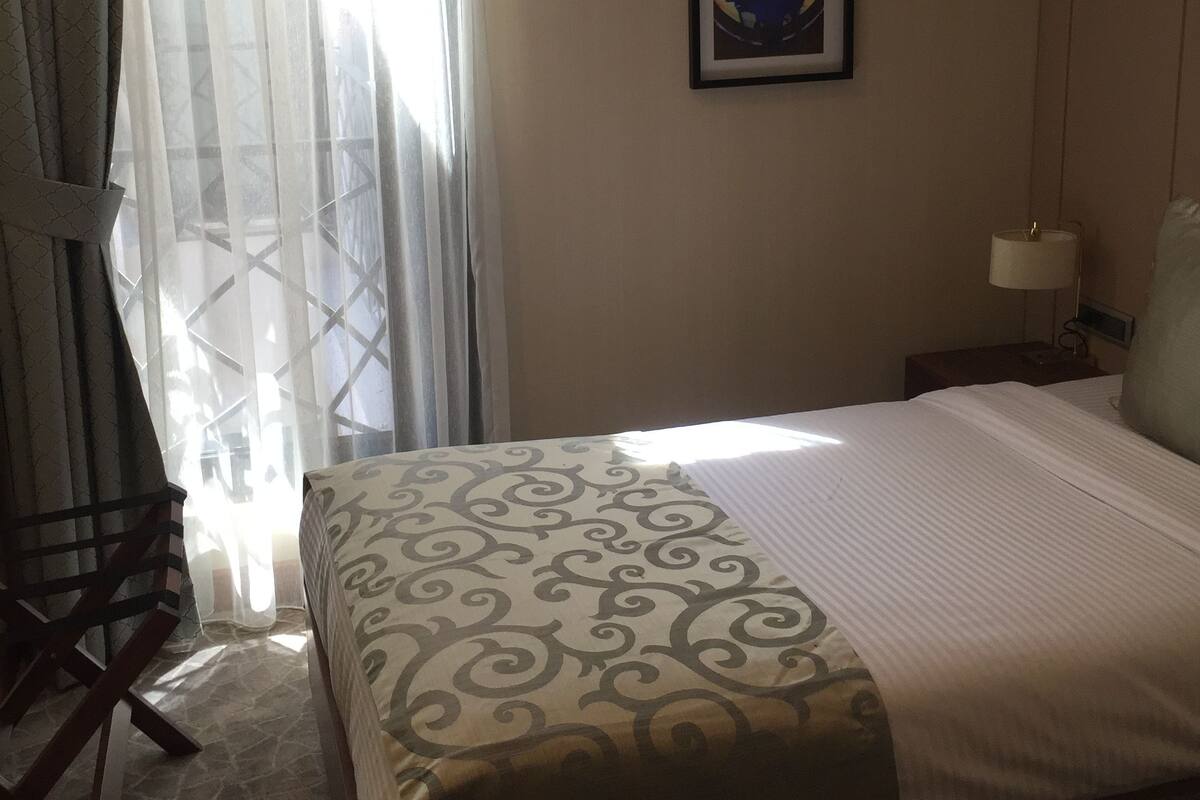 A hotel room with a bed, a chair, a nightstand, a lamp, and a framed picture on the wall.