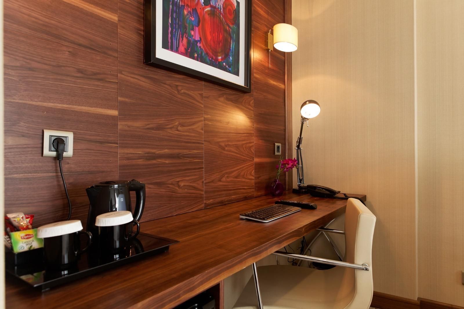 Ein Hotelzimmer mit einem Holztisch, einer Kaffeemaschine, einer Tastatur, einem Telefon und einer Lampe.