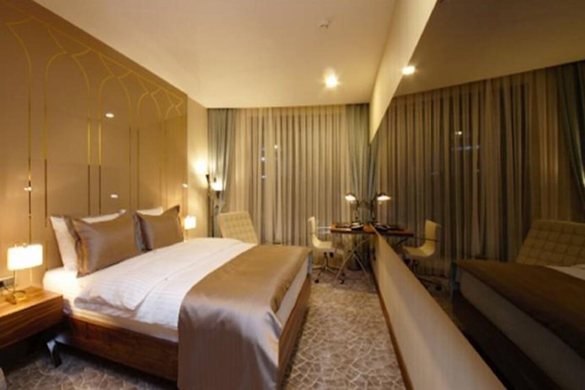 A hotel room with a large bed, bedside tables, a desk, and a seating area with curtains.