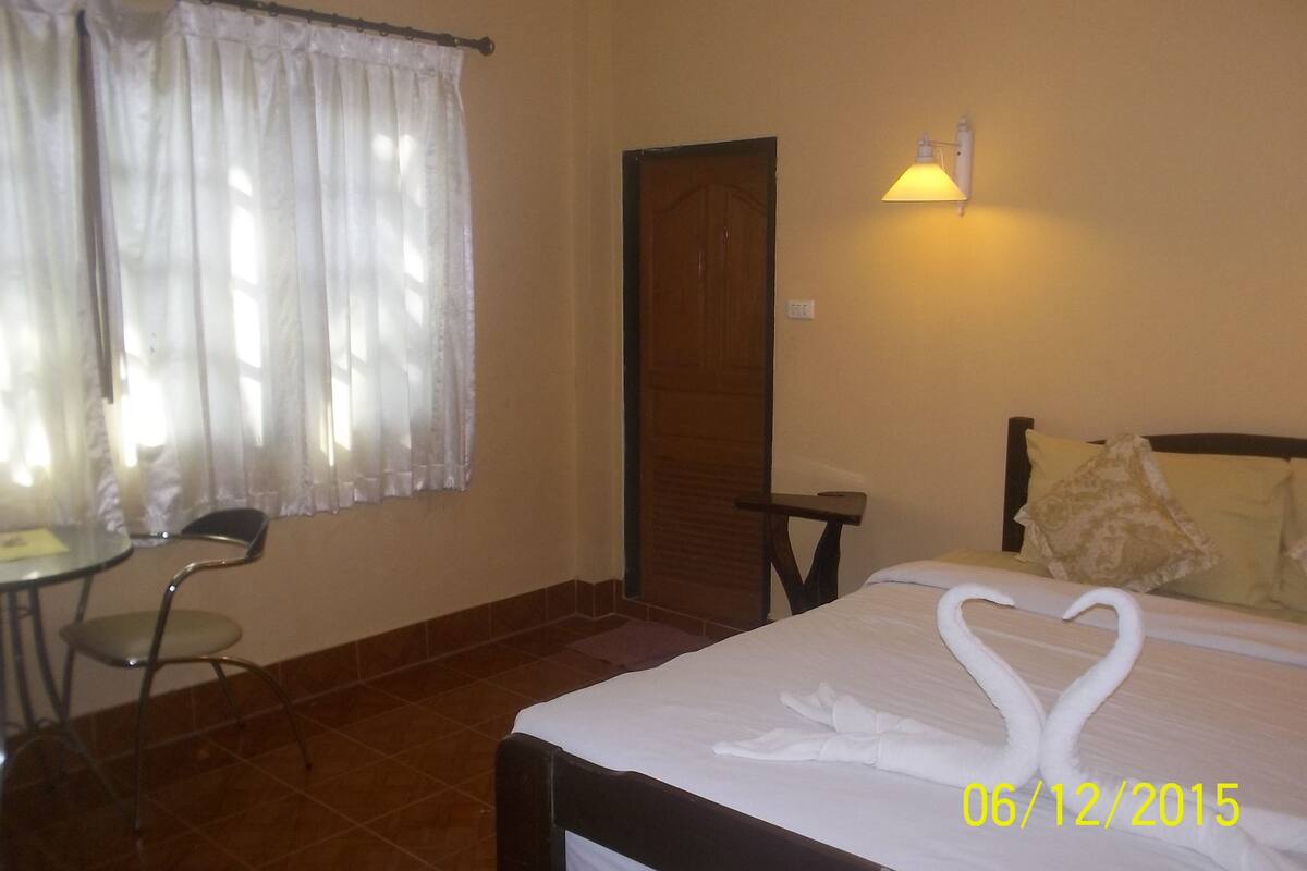 A hotel room with a bed, a chair, a table, a door, and a wall-mounted light fixture.
