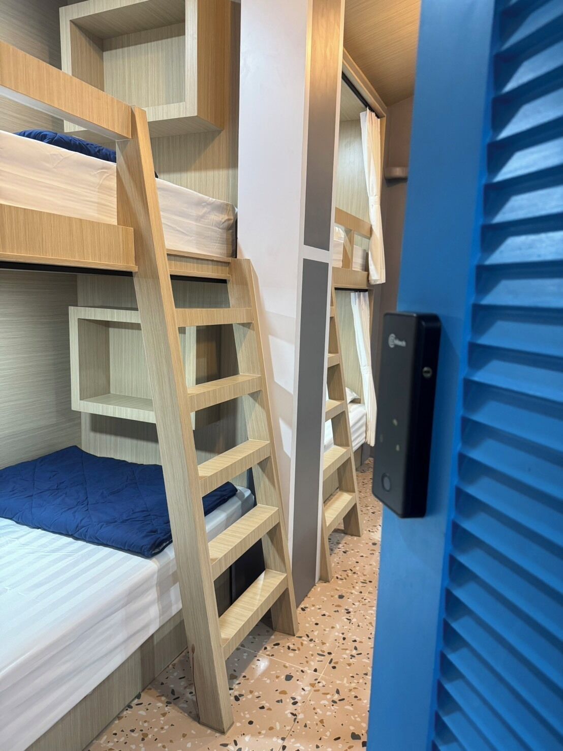 A compact hotel room with bunk beds, a small desk, and a door with a security lock.