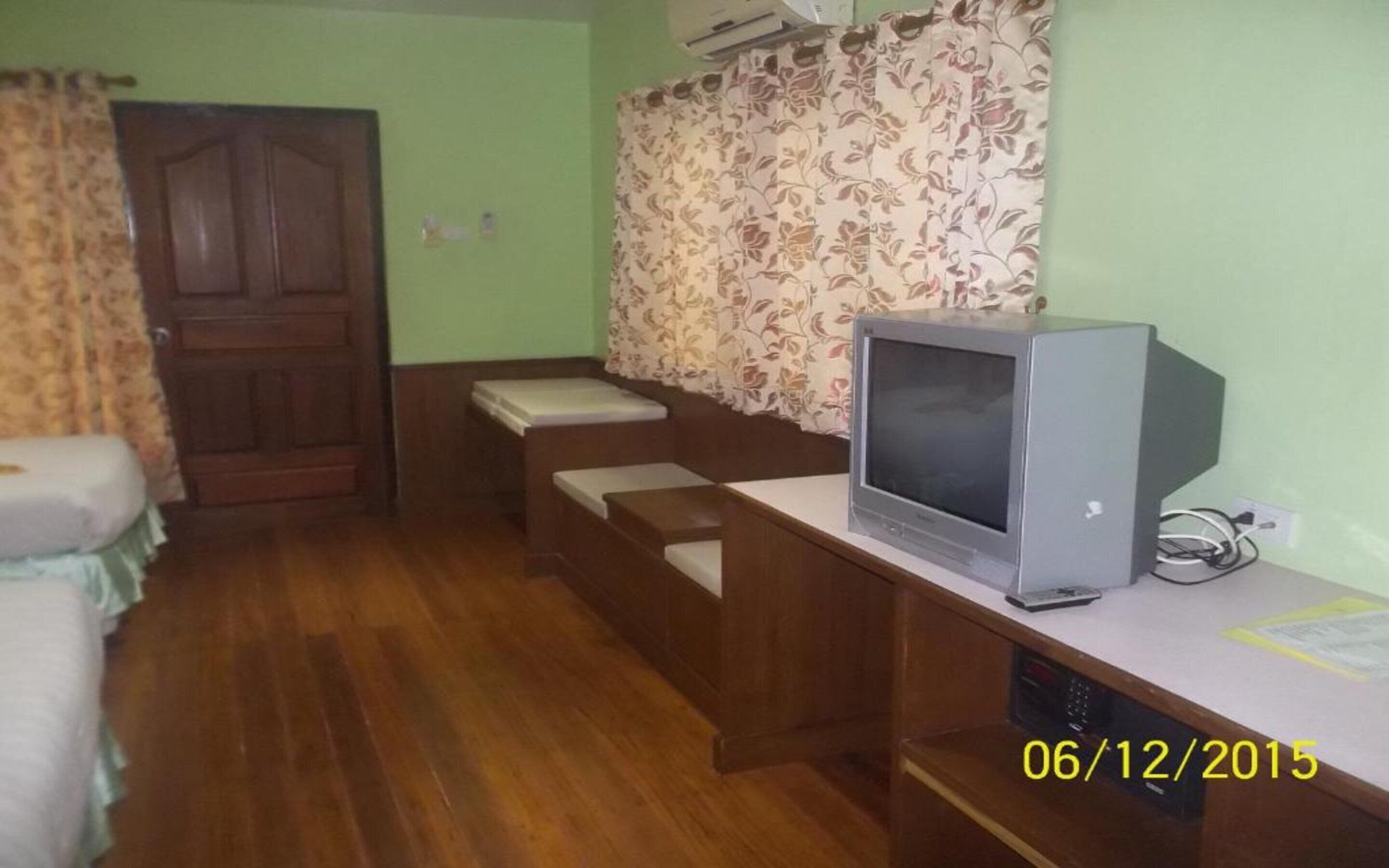 Una habitación con escritorio de madera, televisor, cama y puerta.