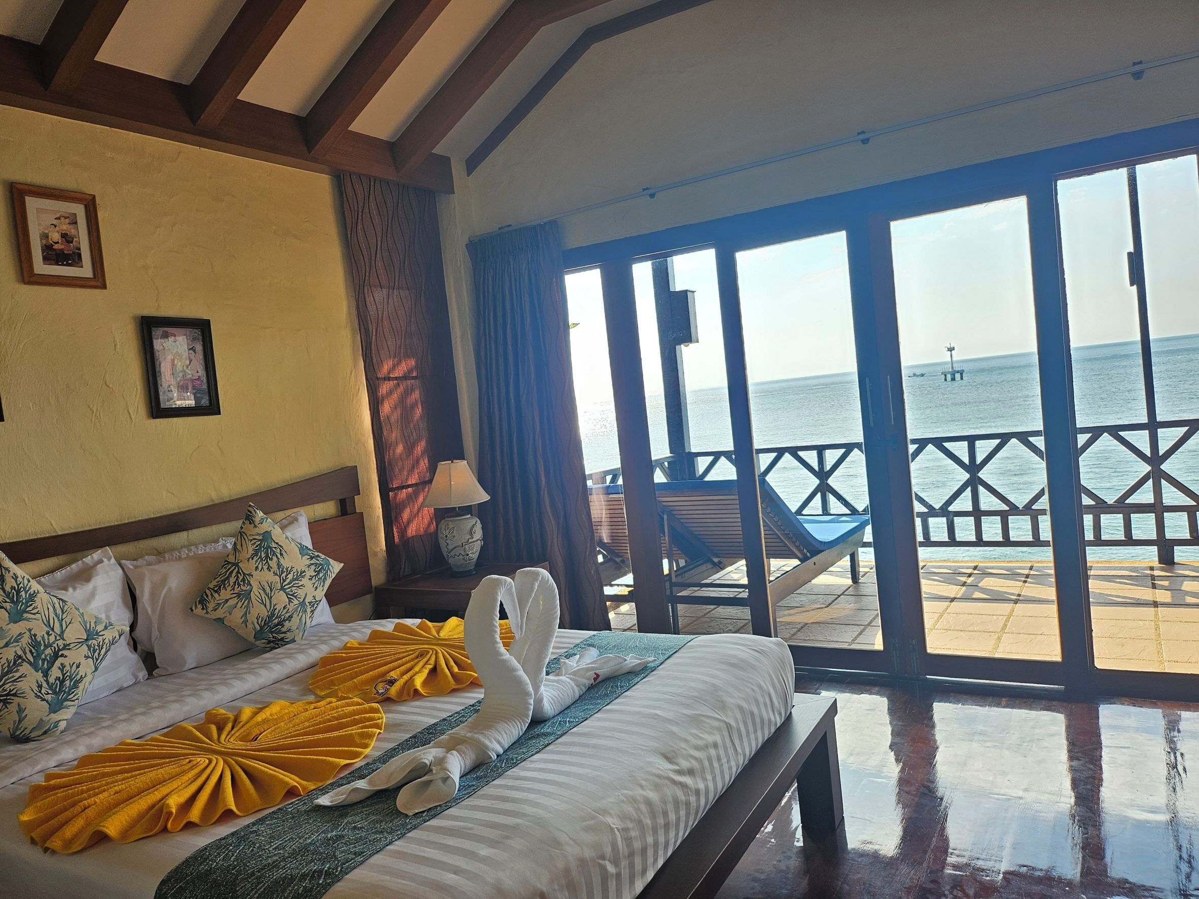 Een hotelkamer met een bed, een bankje, een stoel en uitzicht op zee.