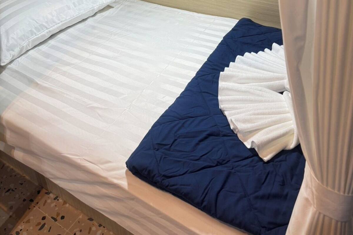 A single bed with a white and blue bedspread, a wooden headboard, and a curtain.