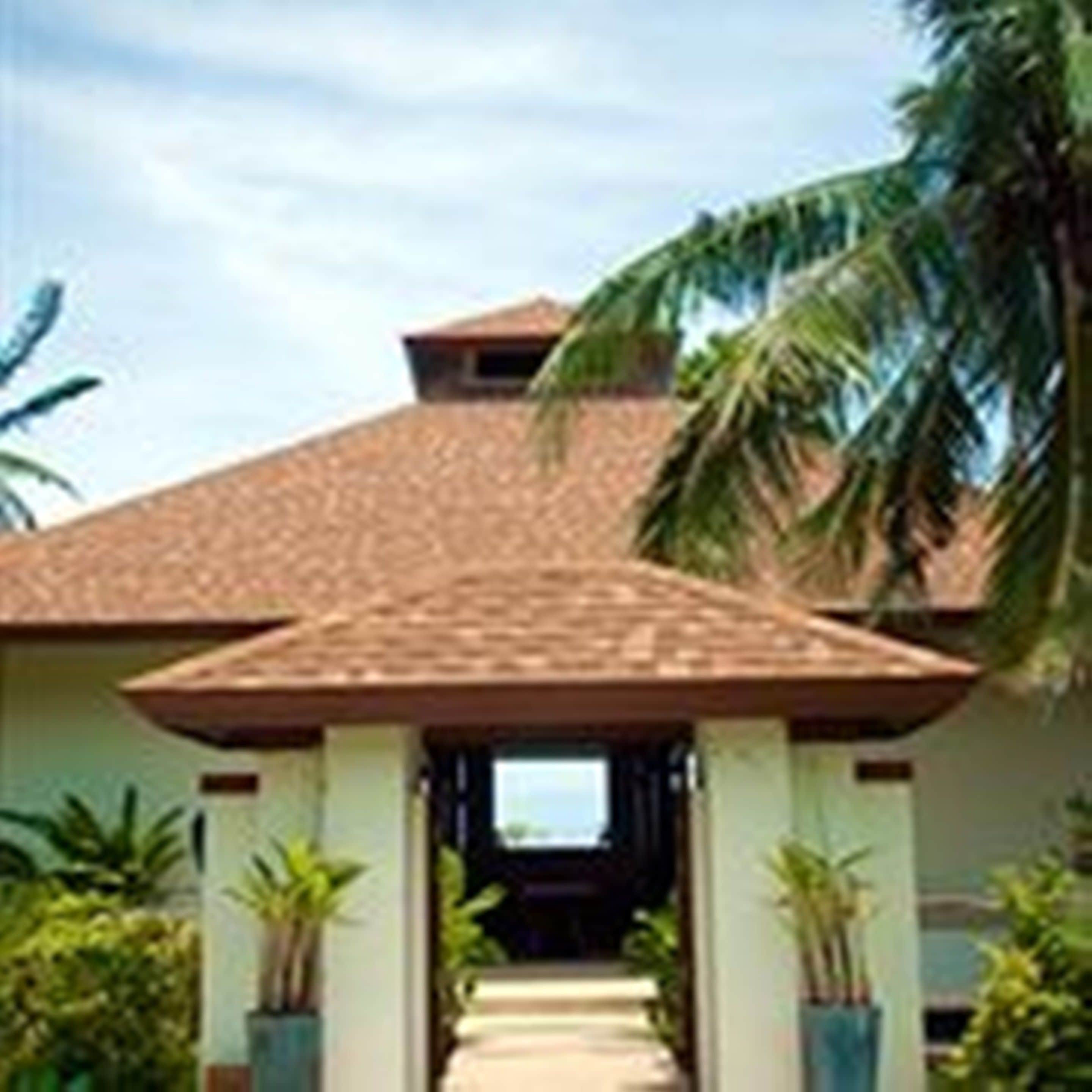 A building with a tiled roof and a covered entrance. There are plants on either side of the entrance.