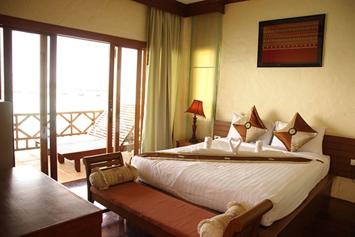 A hotel room with a bed, a bench, a table, and a view of the sea through a sliding door.
