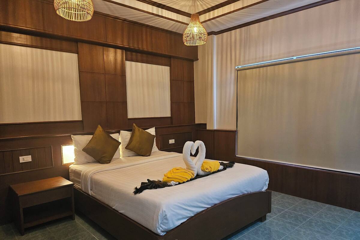 A hotel room with a large bed, wooden headboard, two bedside tables, and a large window with blinds.