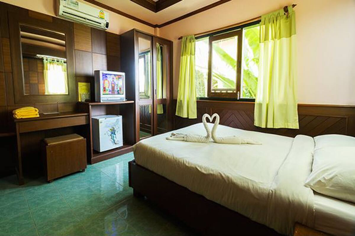 A hotel room with a bed, a television on a stand, a small refrigerator, and a window with curtains.