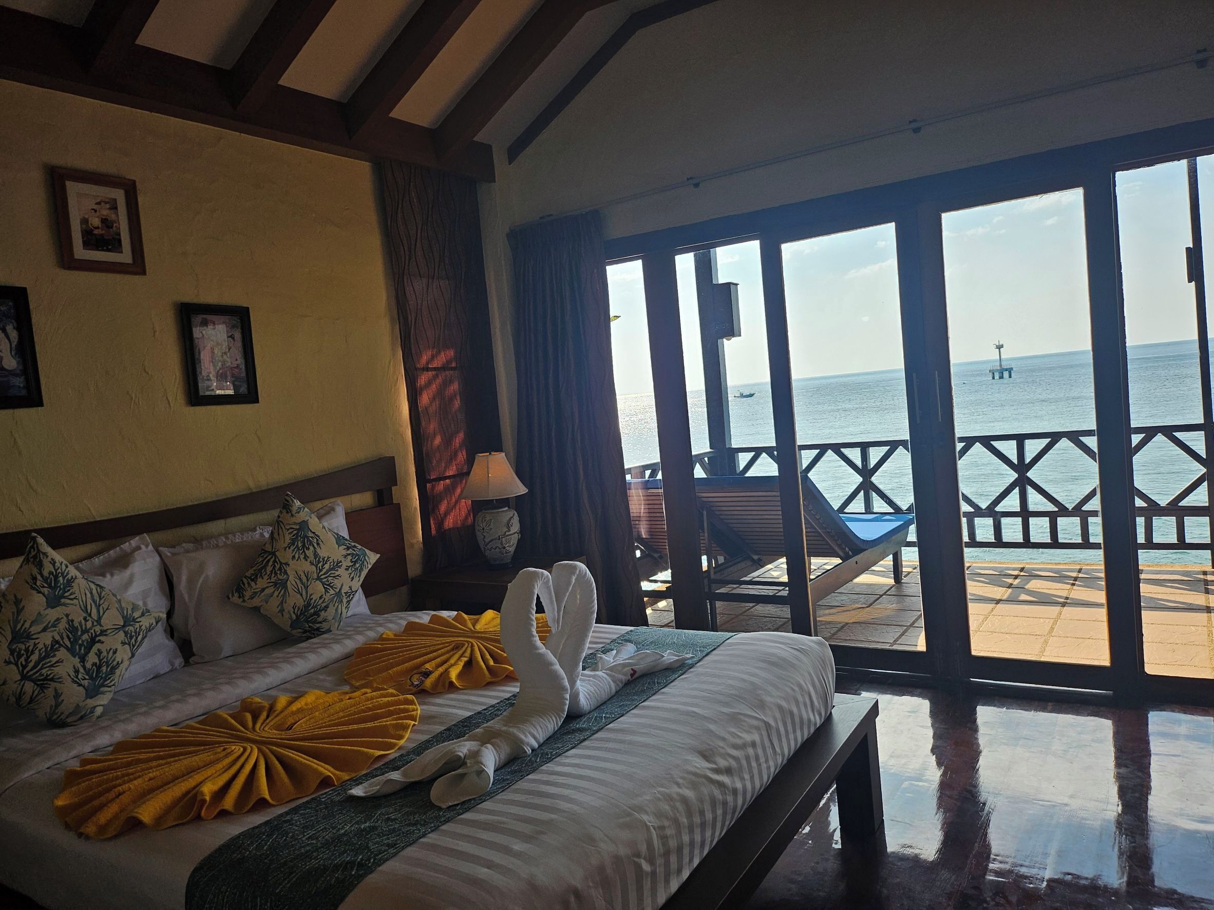 A hotel room with a bed, a bench, and a view of the sea.