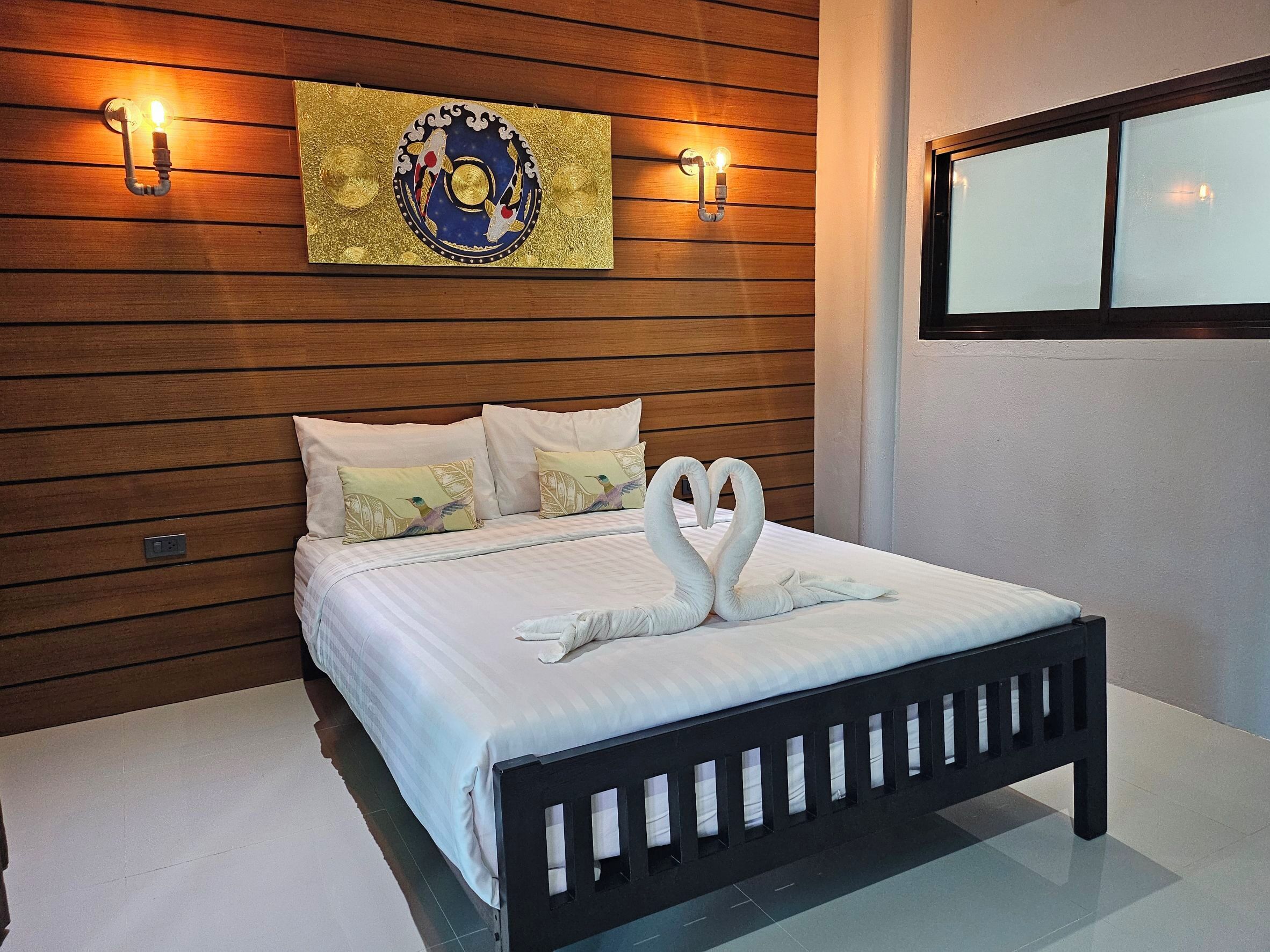 A neatly made bed with two swan-shaped pillows, a wooden headboard, and a wall-mounted artwork above.