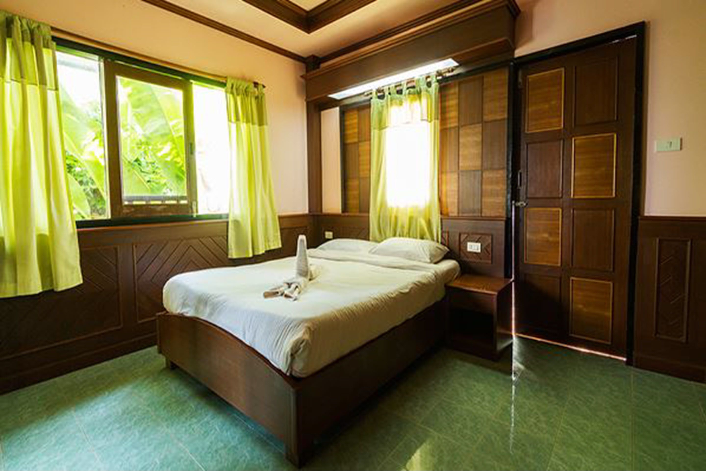 A neatly made bed with a pillow and a folded towel, a nightstand, and a wooden wardrobe with a mirror.