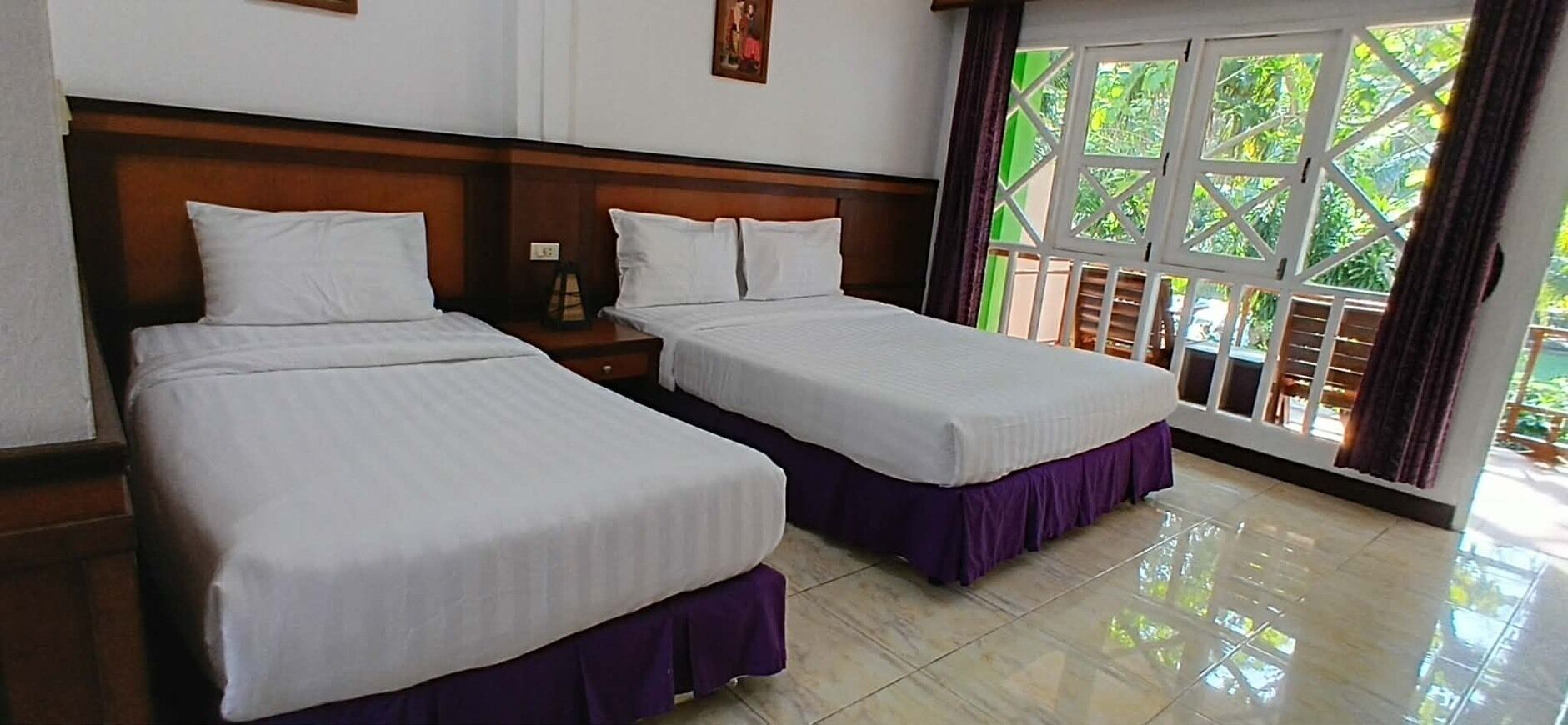 A hotel room with two beds, a wooden headboard, a window with a view of greenery, and a tiled floor.