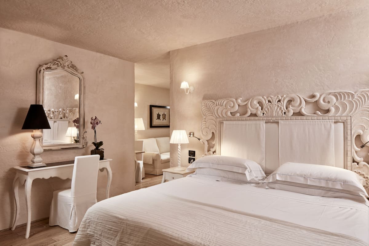 A spacious bedroom with a large bed, a vanity with a mirror, a desk, and a chair.